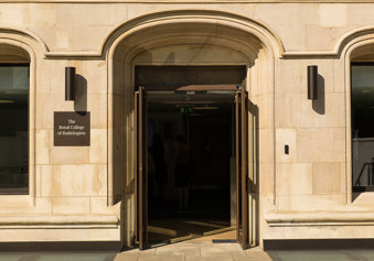 The open main entrance doors to a sandstone building next to a sign naming it as the Royal College of Radiologists. 