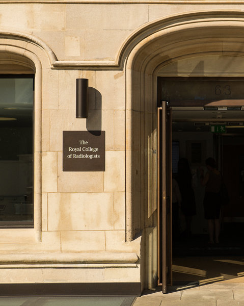 The open main entrance doors to a sandstone building next to a sign naming it as the Royal College of Radiologists. 