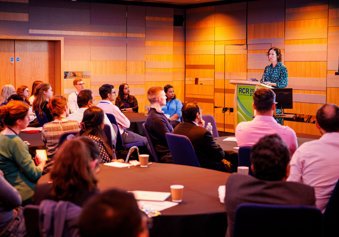Group of attendees at the RCR 2023 conference listening to a speaker standing at a podium