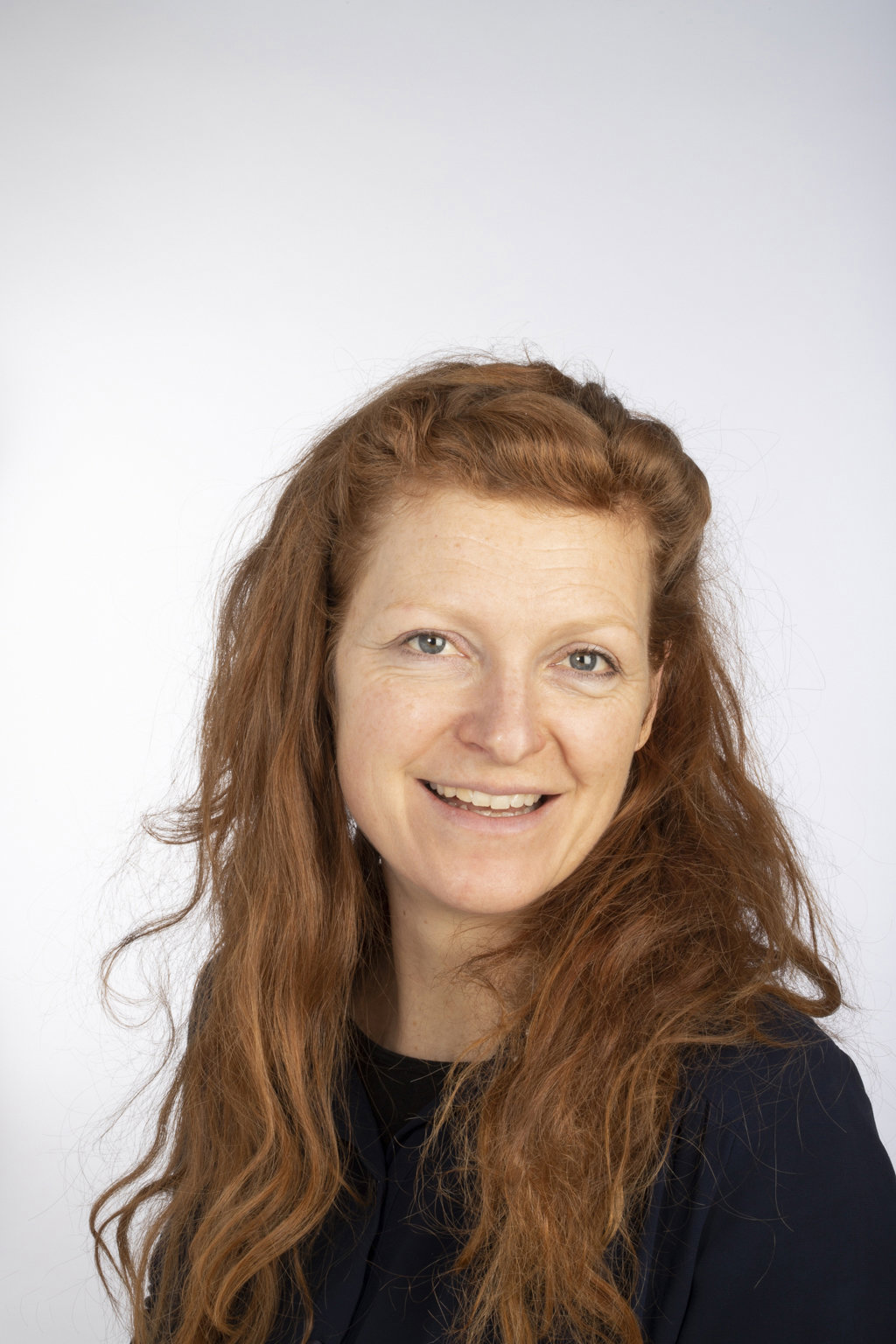 Dr Chloe Mortensen, a head and shoulders portrait of a woman with long red hair, smiling at the camera