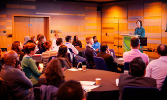 Group of attendees at the RCR 2023 conference listening to a speaker standing at a podium